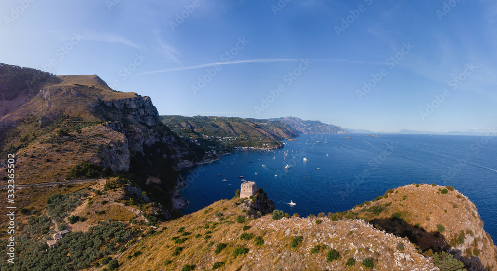 Aerial landscape of Nerano bay. Old signal tower, fortification, rocky shores and blue sea. The city is far on the horizon. Yachts and ships. Water transport movement. Recreation and tourism, Italy Aerial landscape of Nerano bay. Old signal tower, fortification, rocky shores and blue sea. The city is far on the horizon. Yachts and ships. Water transport movement. Recreation and tourism, Italy