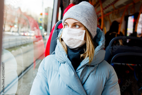 Masked blonde sitting on bus near window during day.