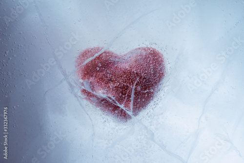 Fotografie Red stone heart frozen in ice with a big cracks, a symbol of love or betrayal or separation