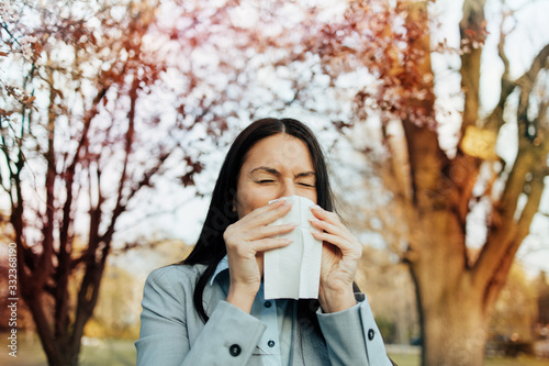 Fotografi Elegant business woman suffering from allergy or seasonal flu standing in city park coughing and sneezing in facial tissue