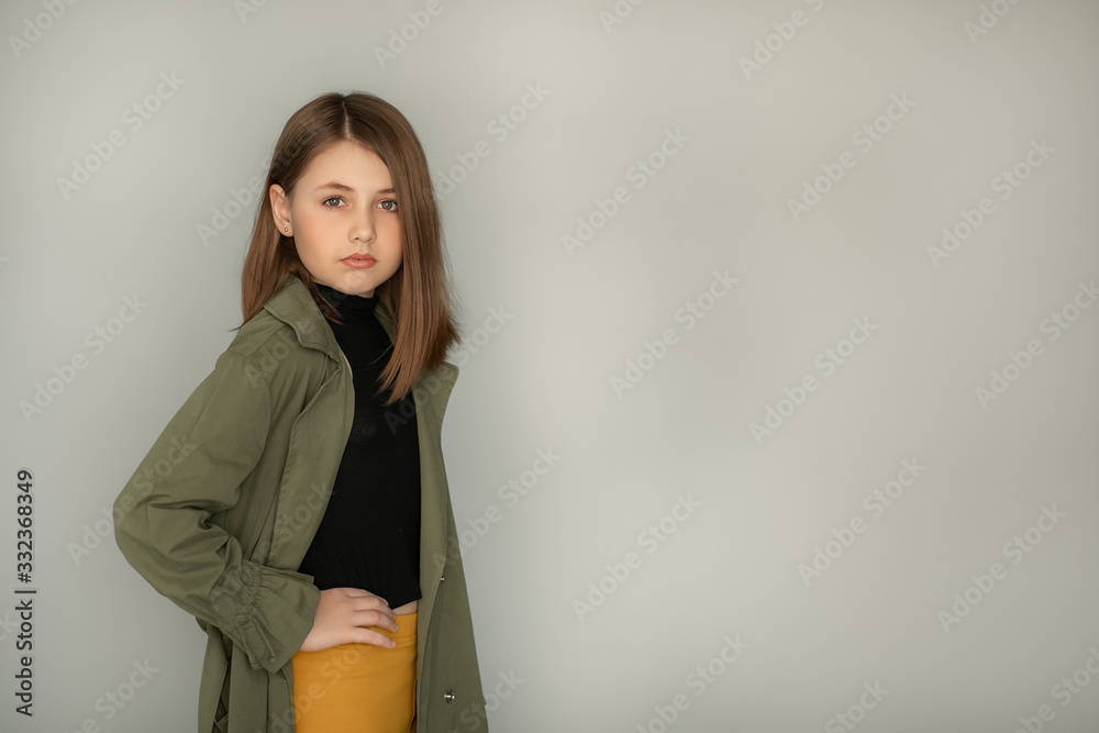 girl in a fashion trench coat and jeans stands against a gray wall. large portrait girl in a fashion trench coat and jeans stands against a gray wall. large portrait