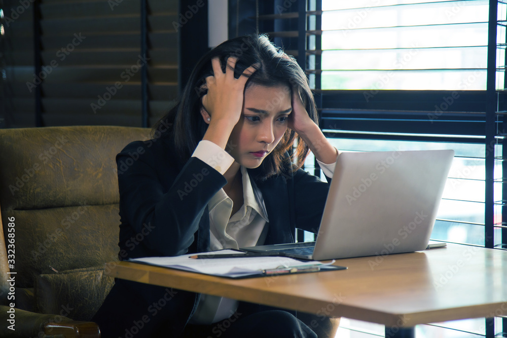Close up portrait stress young Asian businesswoman sitting in front of laptop, She is tense from the problem and holding her head by her hands Close up portrait stress young Asian businesswoman sitting in front of laptop, She is tense from the problem and holding her head by her hands