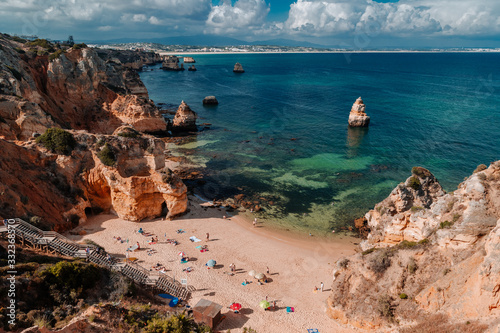 Algarve Portugues beach surrounded by cliffs and emerald water on a hot and cloudy summer day.