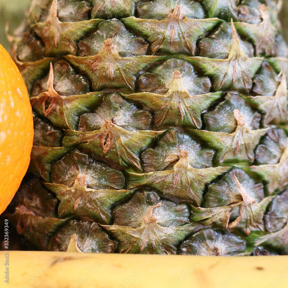 Vertical texture of pineapple skin behind a tangerine on the left and a banana on the bottom Vertical texture of pineapple skin behind a tangerine on the left and a banana on the bottom