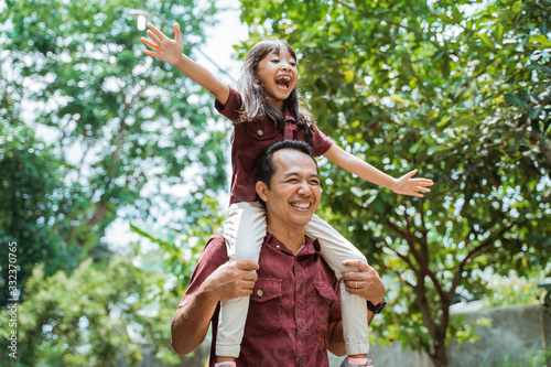 Cheerful father carrying on neck smiling daughter while walking in the park
