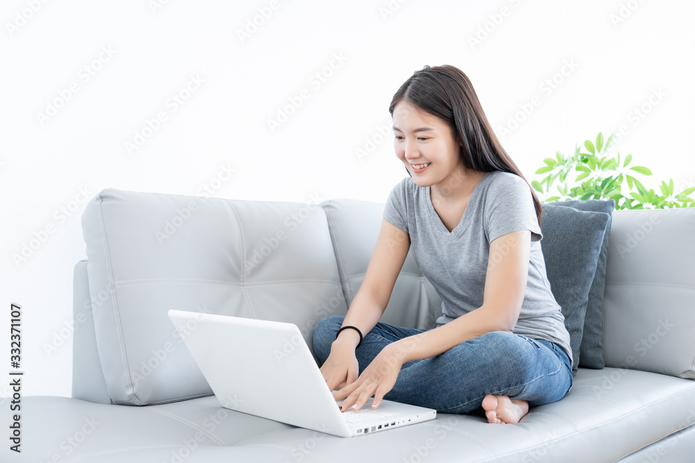 Asian young woman happy and smile using laptop connect internet for working at home and sitting on gray color sofa decoration by plants tree on white background Asian young woman happy and smile using laptop connect internet for working at home and sitting on gray color sofa decoration by plants tree on white background