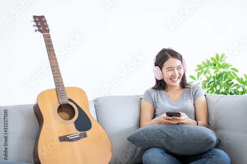 Asian young woman happy and smile listen music or song from music streaming mobile internet and sitting with guitar on gray color sofa on copy space white background