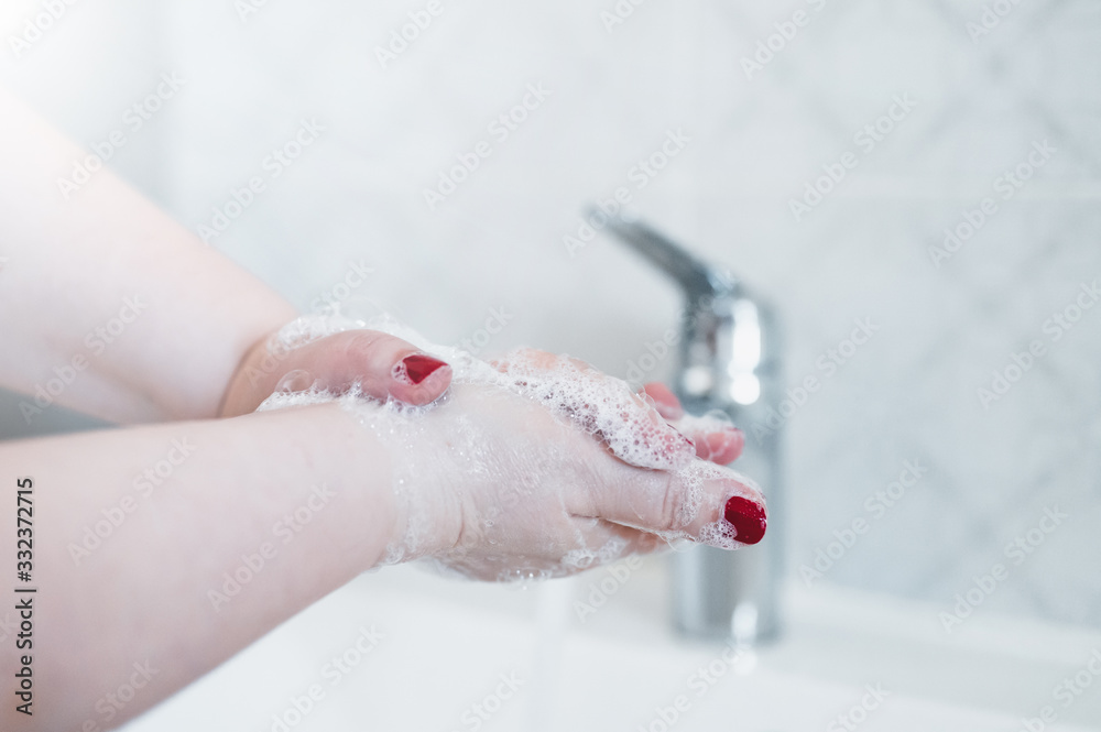 Fototapeta premium Washing hands with soap under the tap with water. Hygiene concept. Beautiful hand and water stream in bathroom.