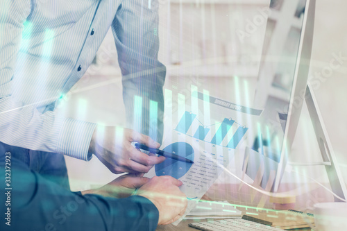 Double exposure of chart with businessman typing on computer in office on background. Concept of hard work.