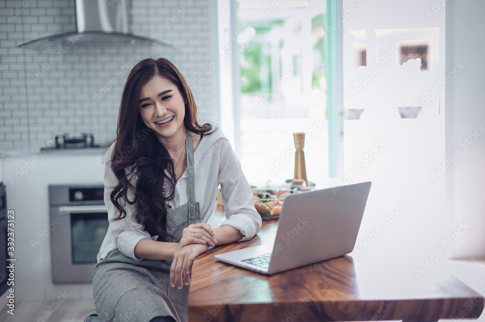 Image of young pretty woman standing in kitchen using computer laptop and cooking with the tomatoes and avocado. Image of young pretty woman standing in kitchen using computer laptop and cooking with the tomatoes and avocado.