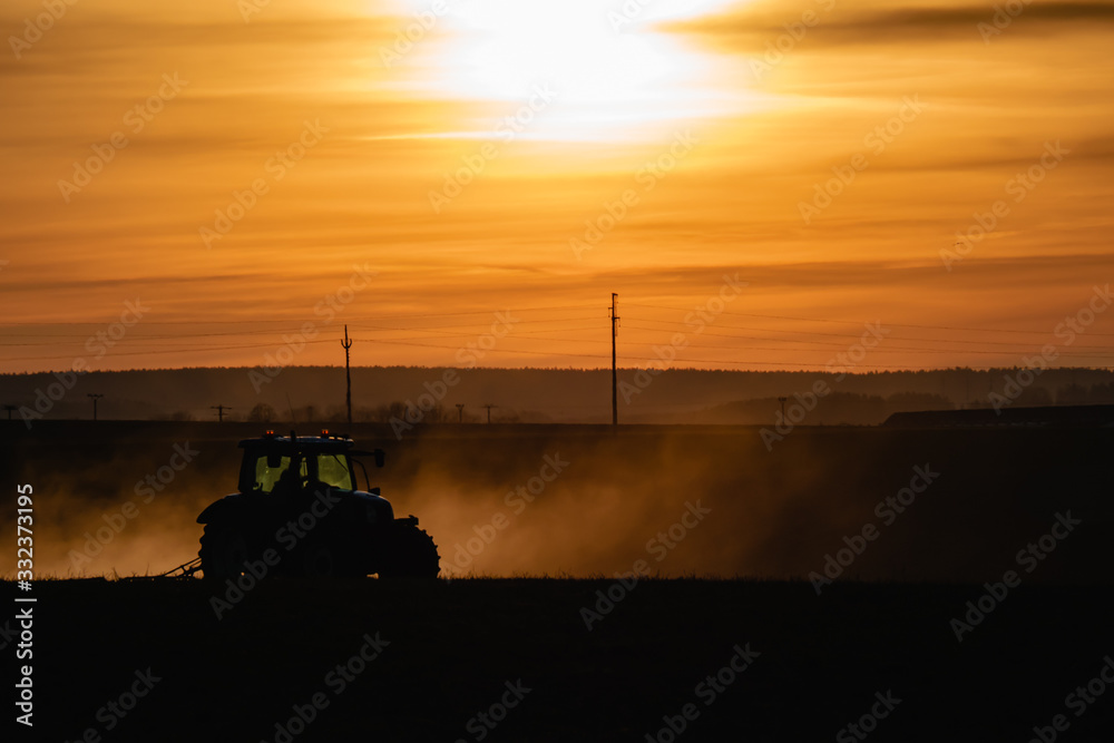Fototapeta premium Tractor silhouette in the field on the orange-yellow sunset