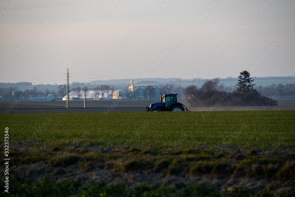 Fototapeta premium Tractor silhouette in the field on the orange-yellow sunset