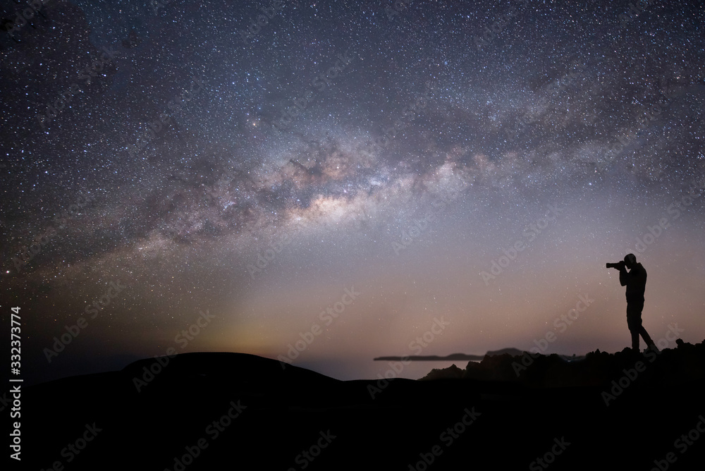 Milky way night panorama with silhuettes of a man intent on photographing the night sky.