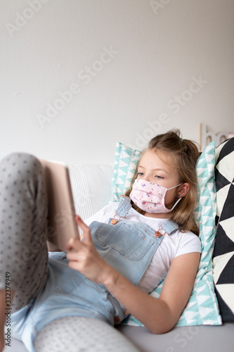 young girl with pink protective mask at home in her room in quarantine with a tablet during corona covid 19 crisis