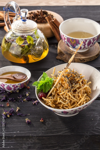 oriental honey dessert chak-chak with and poppy seeds and cup of green tea on black wooden table