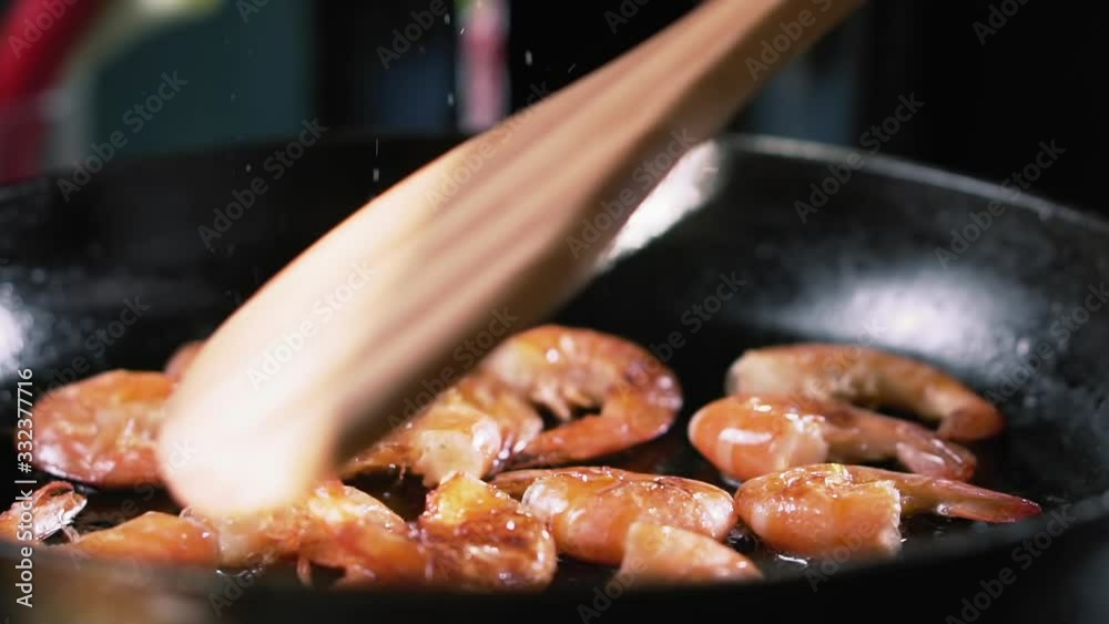 Hand stirs the shrimps in a pan with a bamboo spatula, slow motion. Hand stirs the shrimps in a pan with a bamboo spatula, slow motion.