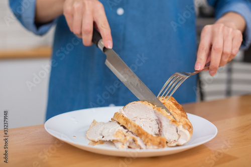 Girl in blue jeans shirt slicing grilled chicken fillet for caesar salad at home kitchen
