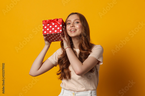 happy young woman with red gift box isolated on yellow background photo