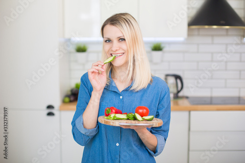 Girl in a blue denim shirt holds in hands plate with fresh vegetables  bell pepper  cucumber  tomato . Vegetarian food concept.