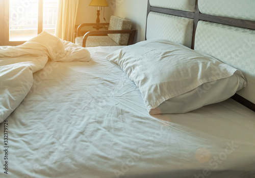 white pillows with messy white bed sheets on empty bed in bedroom for rest and relax in the morning