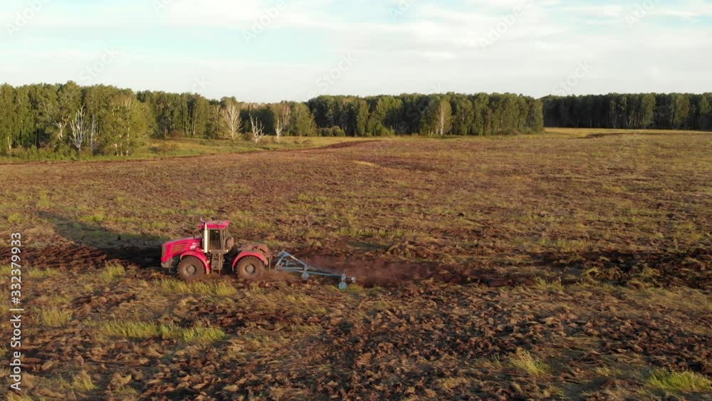 Aerial tracking shot of red farm machinery riding in huge agricultural field and plowing plow grassy soil Aerial tracking shot of red farm machinery riding in huge agricultural field and plowing plow grassy soil