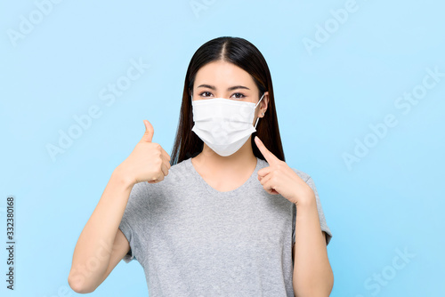 Tela Young Asian woman wearing face mask to protect from COVID-19 and giving thumbs u