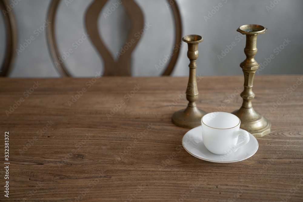 Stylish prop setting with antigue gold candle stick with white ceramic cup with plate setting on real natural wood table / copy space / interior design