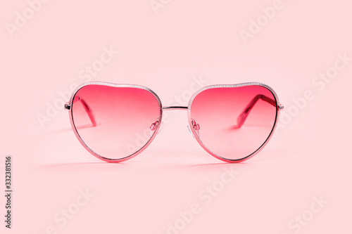 Pink trendy stylish and fashionable slightly heart shaped feminine sunglasses closeup on pink background with copy space. Zine summer and vacation concept