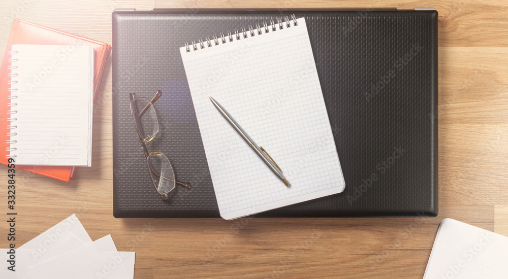 Workplace with laptop, notebook and glasses on a wooden table. Telework. Work from home. Blurred background Workplace with laptop, notebook and glasses on a wooden table. Telework. Work from home. Blurred background