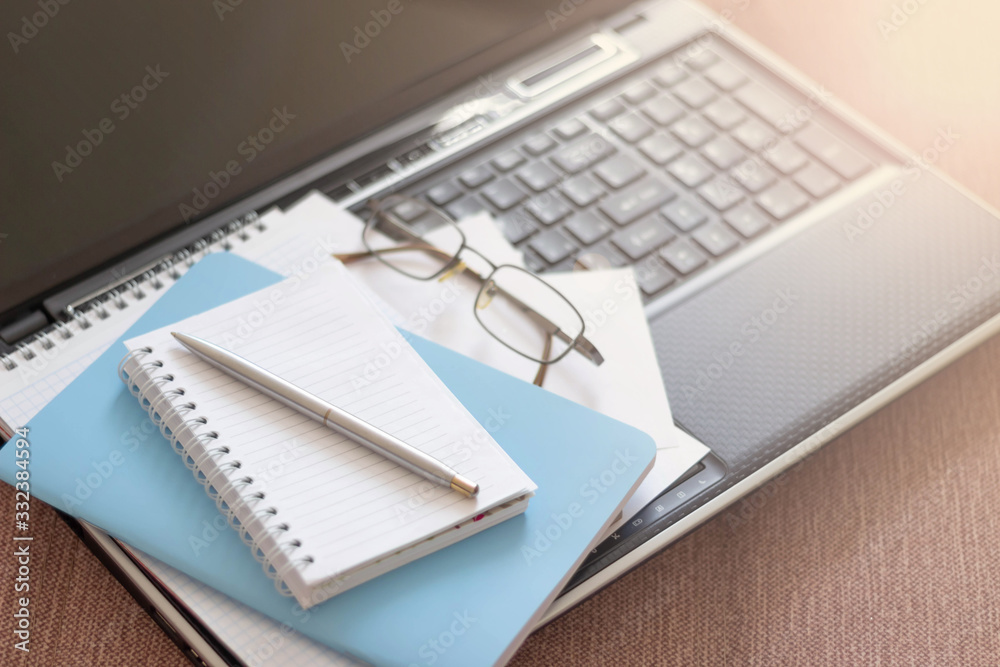 Workplace with laptop, notebook and glasses on a wooden table. Telework. Work from home. Blurred background Workplace with laptop, notebook and glasses on a wooden table. Telework. Work from home. Blurred background