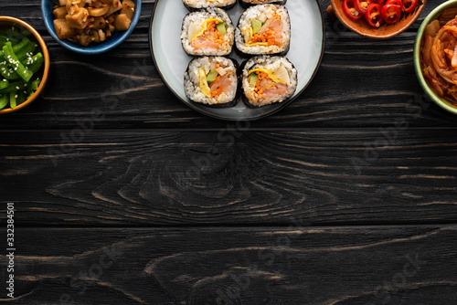 top view of plate with tasty gimbap near side dishes in bowls on wooden surface