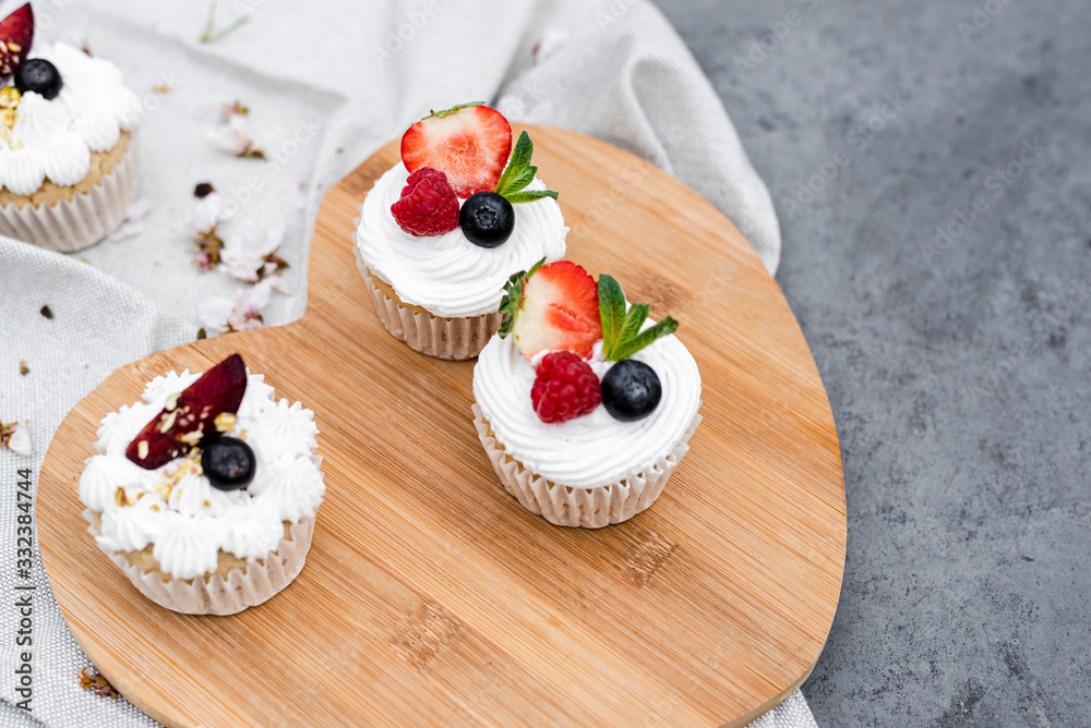 Vegan cupcakes with berries and coconut cream on a wooden board.