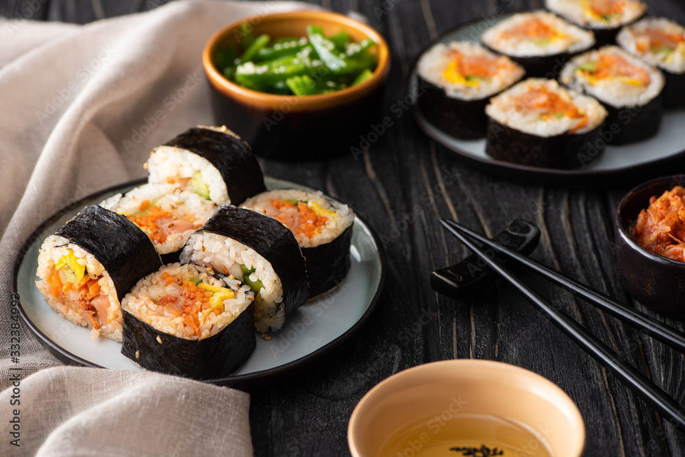 selective focus of tasty rice rolls on plates near chopsticks and korean side dishes on wooden surface selective focus of tasty rice rolls on plates near chopsticks and korean side dishes on wooden surface