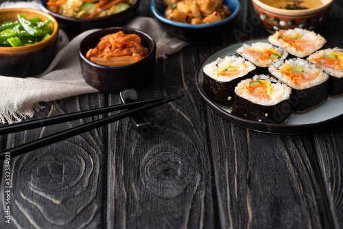 selective focus of korean rice rolls near side dishes, chopsticks and cotton napkin on wooden surface