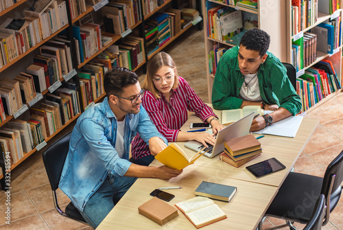 Three young students study in the school library and using laptop for researching online.