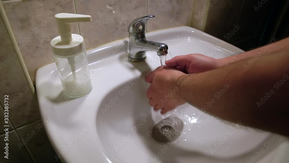 Young man washes his hands in the bathroom with an old washbasin. The Man thoroughly washes hands from bacteria in the washroom. Young man washes his hands in the bathroom with an old washbasin. The Man thoroughly washes hands from bacteria in the washroom.