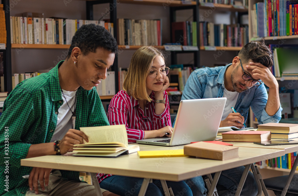 Three young students study in the school library and using laptop for researching online. Three young students study in the school library and using laptop for researching online.