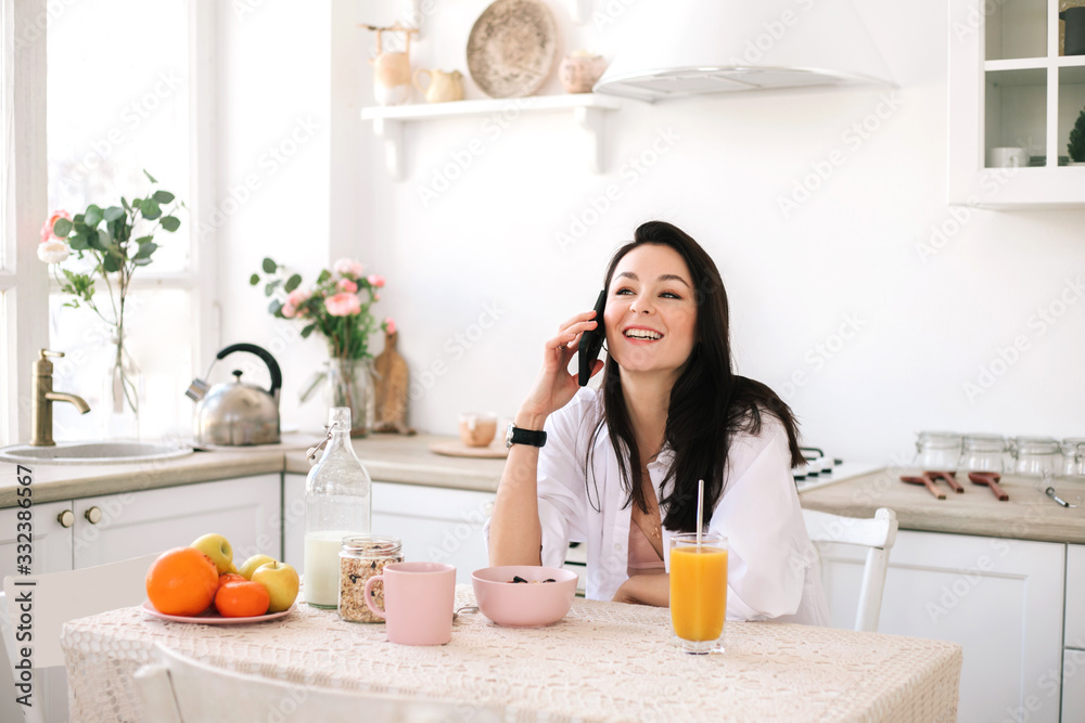 Young beautiful woman using mobile phone while breakfast in kitchen.
