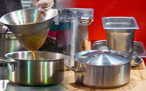 The cuisine of the restaurant. Pots and gastronomic containers in the kitchen. The person is filtering the sauce. Concept - work in a restaurant. Chef's career. Concept - restaurant business.