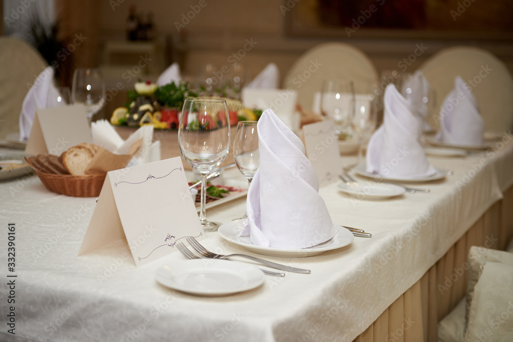 Table set with blank guest card, plate with serviette and cutlery on table, copy space. Place setting at wedding reception. Table served for wedding banquet in restaurant
