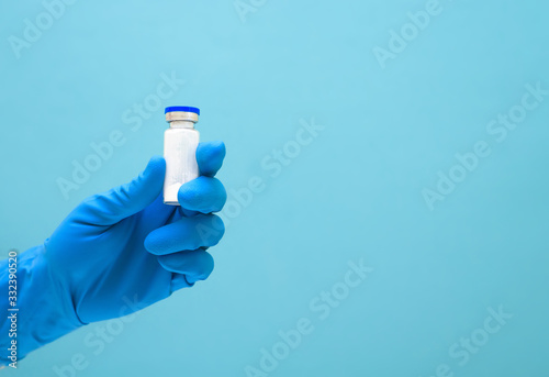 virus vaccine in hand in a medical blue glove against coronavirus on a blue background. space for text. clinical therapy of the epidemic. taking care of people's health