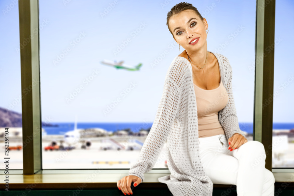 Woman sitting on window sill and red suitcase with summer hat. Airport background and copy space for your decoration. 