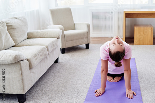 Portrait of young woman practicing yoga at home indoor, copy space. Girl stretching on mat, full length. Relaxing and doing yoga. Wellness and healthy lifestyle