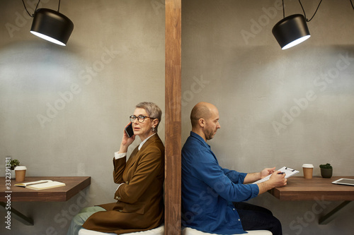 Minimal side view portrait of two adult people separated by wall while sitting in separate cafe booths, copy space photo