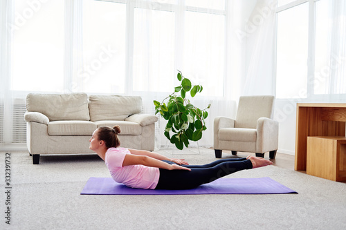 Portrait of young woman practicing yoga at home indoor, copy space. Girl stretching on mat, full length. Salabhasana (Locust pose). Wellness and healthy lifestyle photo