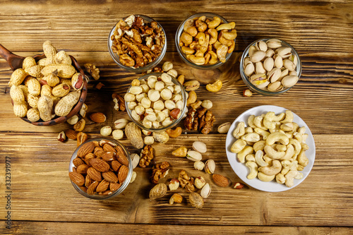 Assortment of nuts on wooden table. Almond, hazelnut, pistachio, peanut, walnut and cashew in small bowls. Top view. Healthy eating concept