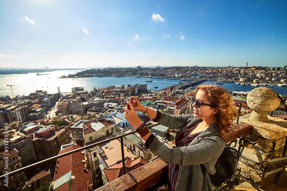 A beautiful girl tourist taking photo on her smartphone and enjoying the view of  historical center of Istanbul from the top of the Galata Tower