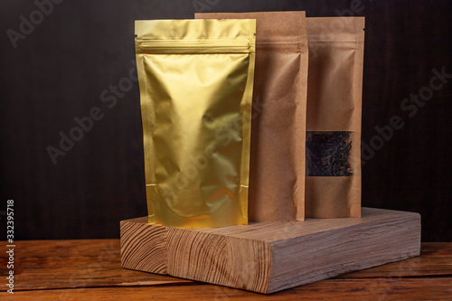 Paper and foil pouch bags with coffee beans and tea leaves on dark wooden background. Packaging for foods and goods brand mockup, shopping offer, sales. Weight products packs with clasps and windows.