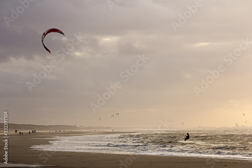 View of the north sea beach on a windy winter day at sunset, people, kitesurfing. Noordwijk, the Netherlands