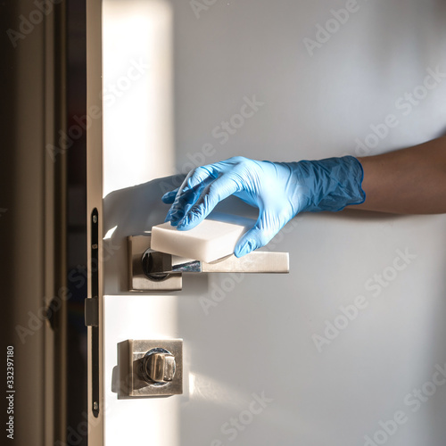 A hand in a latex blue glove cleans door handles during quarantine. The concept of self-isolation during a pandemic and epidemic.